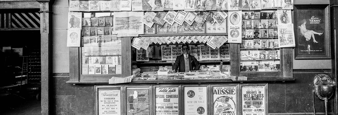 Black and white photograpgh of man standing behind Newspaper stand at Spencer St train station, July 1930