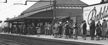 Black and white photo of people waiting on a railway station platform