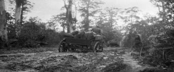 black and white image of men with horse and cart walking through muddy track in the bush