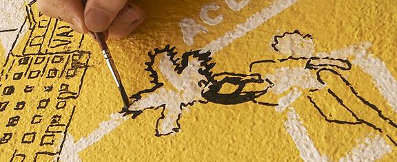 Close up of a hand painting a picture on a yellow wall